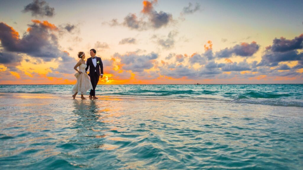 tropical destination wedding A bride and groom on their wedding day, stroll along an idyllic tropical beach at sunset.